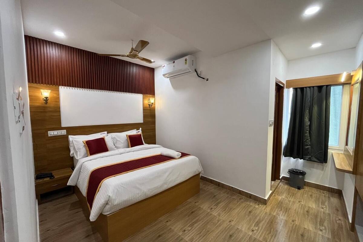 Hotelkamer met een bed, houten vloer, plafondventilator, airconditioning en een raam met gordijnen.