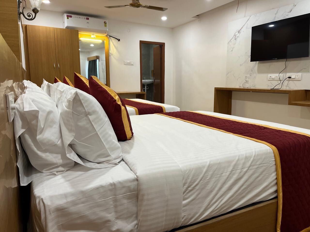 Una habitación de hotel con cama, televisor montado en la pared y ventilador de techo.
