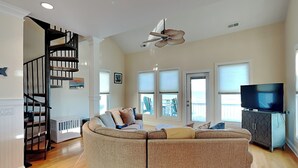 A spacious living room with a curved sectional sofa, a ceiling fan, and a television on a cabinet. - Surf's Up (Carolina Beach)