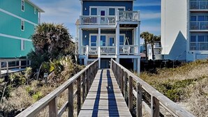 A multi-story building with balconies, a wooden boardwalk leading to it, and a clear sky. - Surf's Up (Carolina Beach)