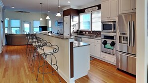 A modern kitchen with a central island, bar stools, stainless steel appliances, and a view of the ocean. - Surf's Up (Carolina Beach)