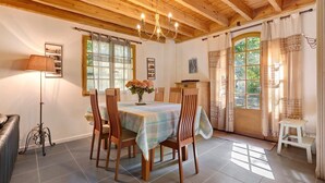 A dining area with a wooden ceiling, a chandelier, a table with a tablecloth, wooden chairs, and a vase with flowers.