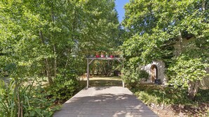 A wooden pathway leading to a pergola with potted plants.