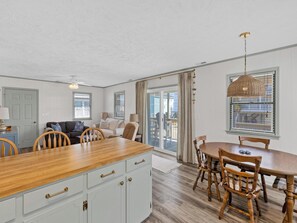 Une cuisine dotée d’un îlot central en bois, de meubles blancs et d’un coin repas avec des chaises et une table en bois.
