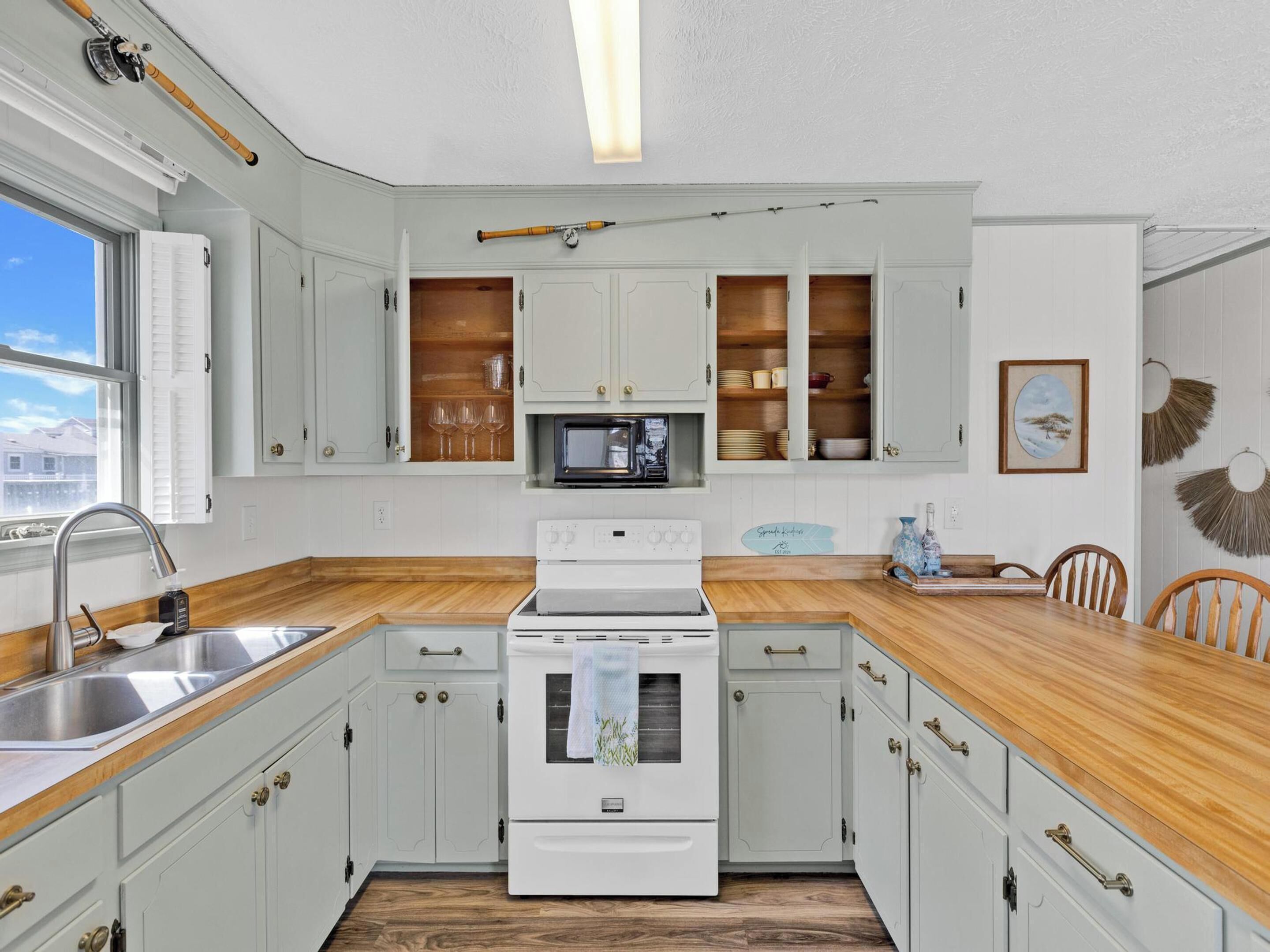 A kitchen with white cabinets, a wooden countertop, a built-in microwave, and a stove.