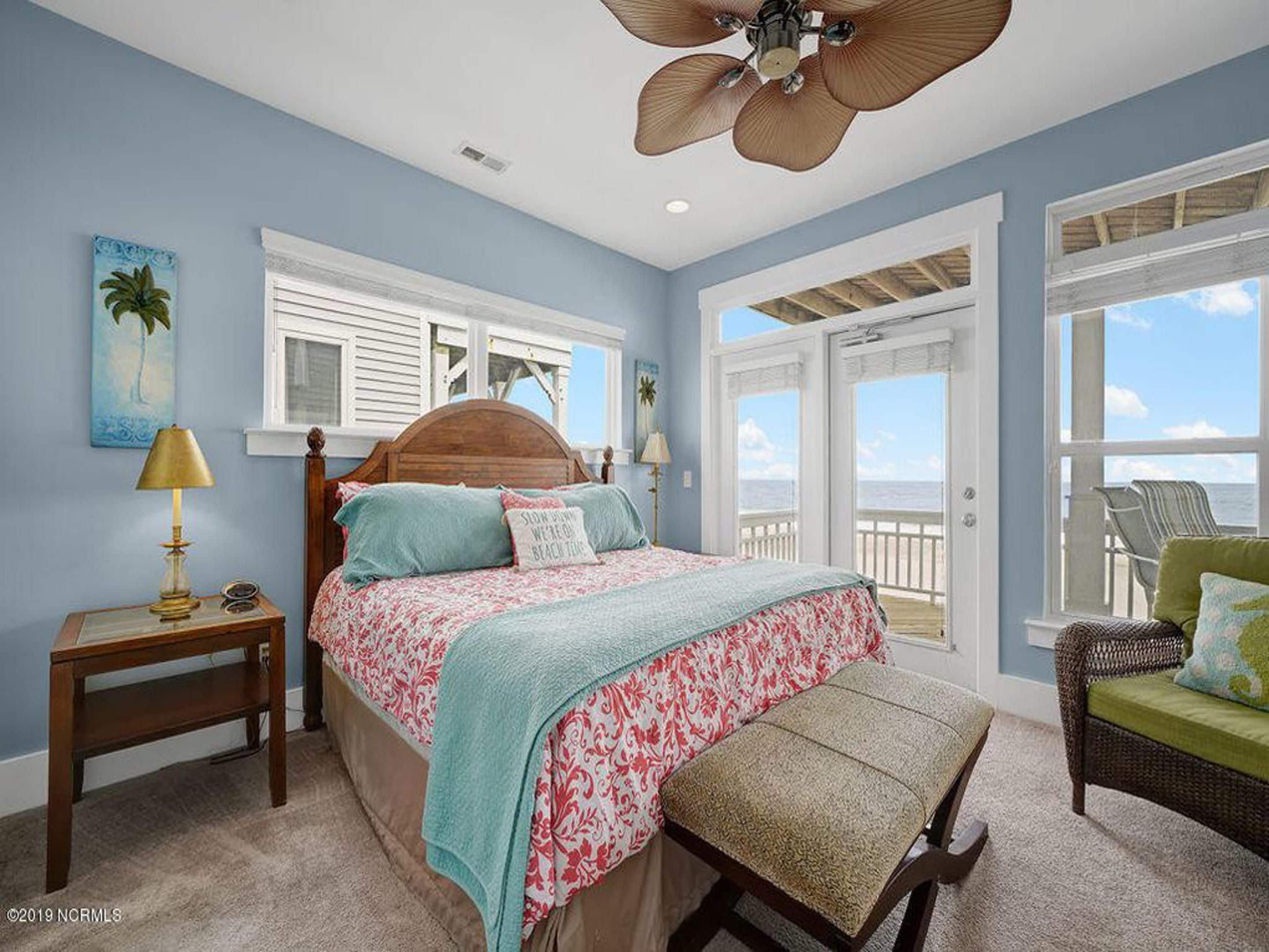 A bedroom with a bed, a nightstand, a chair, and a view of the ocean.