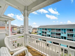 A coastal hotel with a white balcony, white chairs, and a view of turquoise buildings. - Dolphin Watch (Carolina Beach)