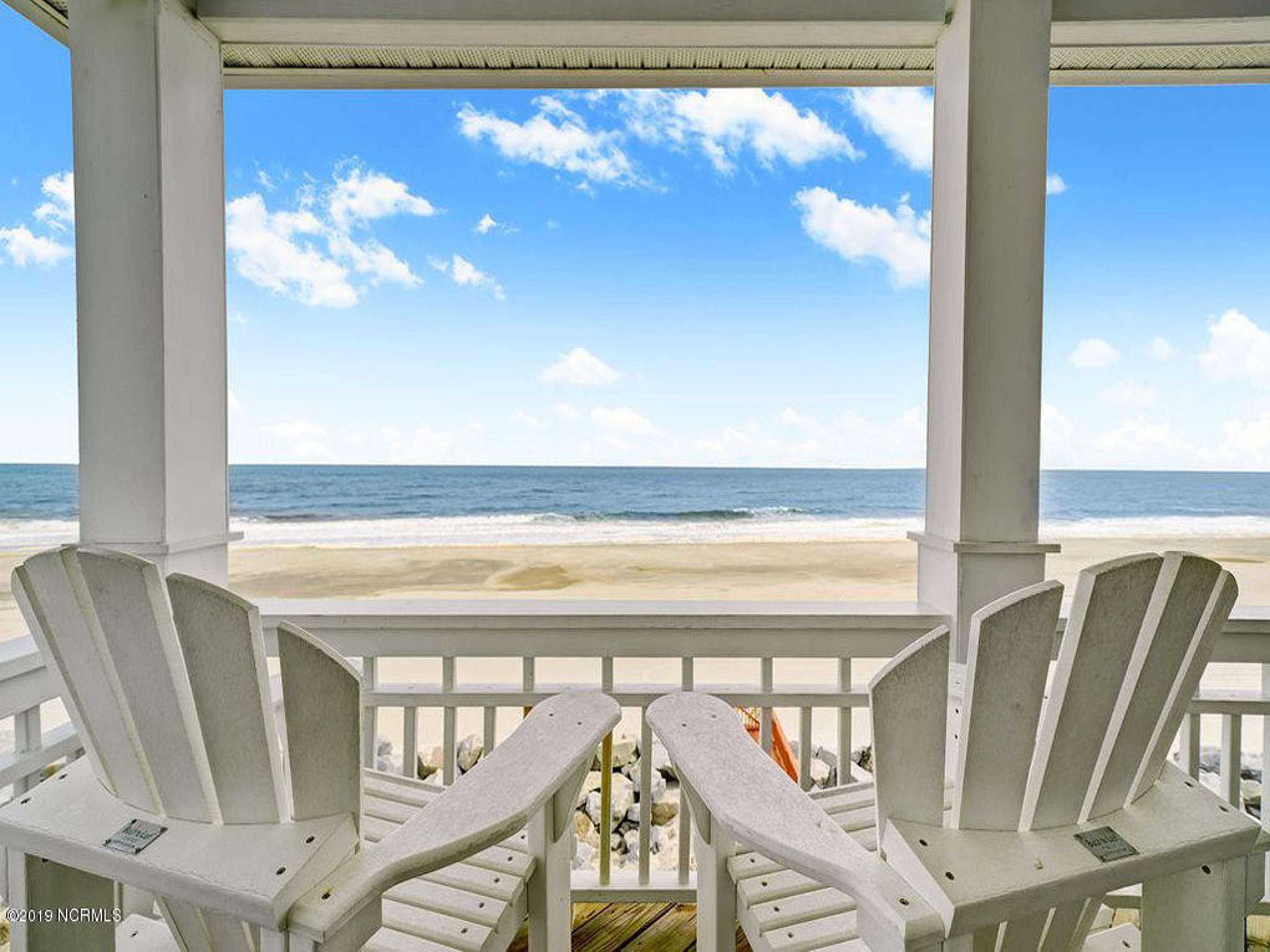 Eine überdachte Terrasse mit zwei Adirondack-Stühlen, die auf einen Strand ausgerichtet sind.