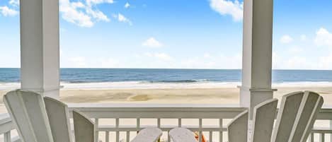 A covered deck with two Adirondack chairs facing a beach.