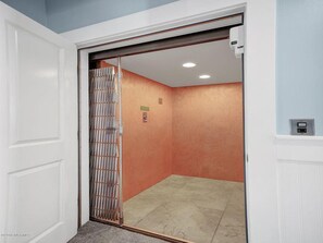 Un couloir étroit, avec une porte blanche sur la gauche et un portail en métal sur la droite.