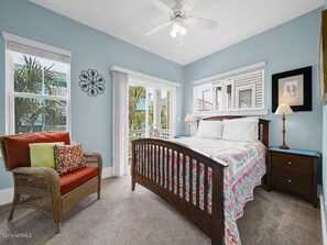 Une chambre à coucher comprenant un lit, une chaise, une table de chevet et un ventilateur de plafond.