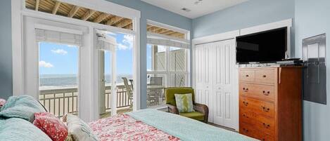 A bedroom with a bed, a dresser, a TV, and a balcony with a view of the ocean.