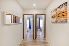 A hallway with wooden flooring, a painting of a cityscape, and a mirrored wall. - Charming Marsaskala Stay |Balcony & Seafront Walks (Marsaskala)