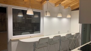Une cuisine moderne avec un plan de travail blanc, quatre suspensions et une fenêtre agrémentée de rideaux à motifs.