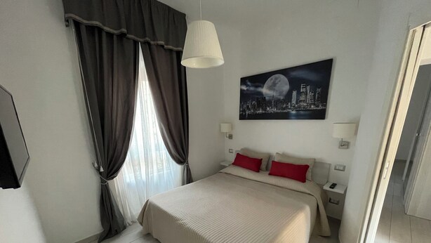 Une chambre d’hôtel avec un lit, des rideaux, un tableau représentant un paysage urbain et une table de chevet.