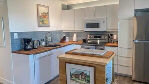 A modern kitchen with white cabinets, a microwave, a stainless steel refrigerator, and a wooden island with a picture frame.