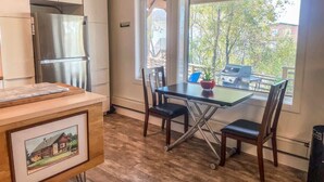A kitchen with a stainless steel refrigerator, a dining table with four chairs, and a window with a view of a backyard.