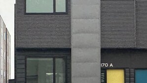 Un edificio moderno con techo plano, dos ventanas visibles y una puerta marcada con el número '170 A'.
