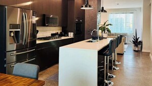 Una cocina moderna con electrodomésticos de acero inoxidable, una isla central, iluminación colgante y vistas al área de estar.