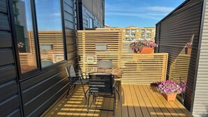A wooden deck with a chair and a table, a potted plant, and a view of buildings in the background.