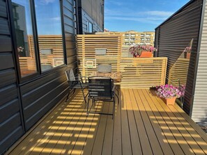 Eine Holzterrasse mit einem Stuhl, einem Tisch, einem Topfpflanze und Blick auf Gebäude im Hintergrund.