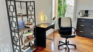 Une pièce comprenant un bureau, un fauteuil de bureau, une bibliothèque et une fenêtre agrémentée de plantes.