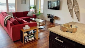 Un salon moderne avec un canapé rouge, une table basse, une bibliothèque, un téléviseur et une décoration sur le thème du surf.