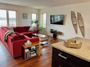Ein modernes Wohnzimmer mit einem roten Sofa, einem Couchtisch, einem Bücherregal, einem Fernseher und einer Surfbrett-Dekoration.