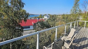 Une terrasse avec des chaises, une rambarde et une vue sur un bâtiment aux toits rouges et des arbres.