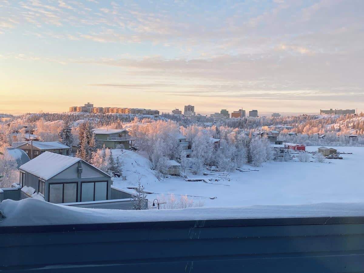 Een besneeuwde woonwijk met huizen, een klein gebouw en een verafgelegen stadsachtergrond.