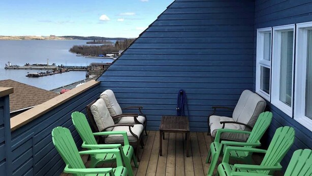Une terrasse avec des chaises vertes et une table, donnant sur une étendue d’eau et un quai.