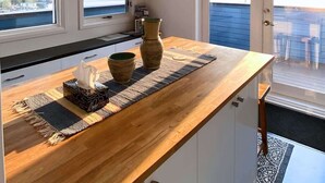 Une cuisine moderne avec un plan de travail en bois, des luminaires suspendus et une vue sur l’extérieur.