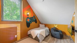 Quarto com teto inclinado, uma cama, poltrona de saco e televisão na parede, além de janela com persianas.