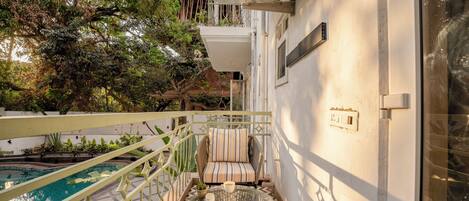 A balcony with a glass table, cushioned seating, and a pool.