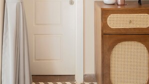 A room with a closed door, a television on a wooden cabinet, and a vase with flowers. - Staymaster Solintra 2BHK C101 (Verem)