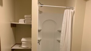 Ein Badezimmer mit Toilette, einer Dusche mit Glastür und Regalen mit gefalteten Handtüchern.