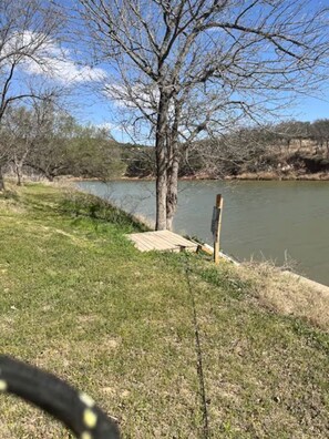 A grassy area with a wooden dock extending into a body of water, surrounded by trees and a clear sky. - Charming 1-bedroom cabin in peaceful Weatherford getaway (Weatherford)