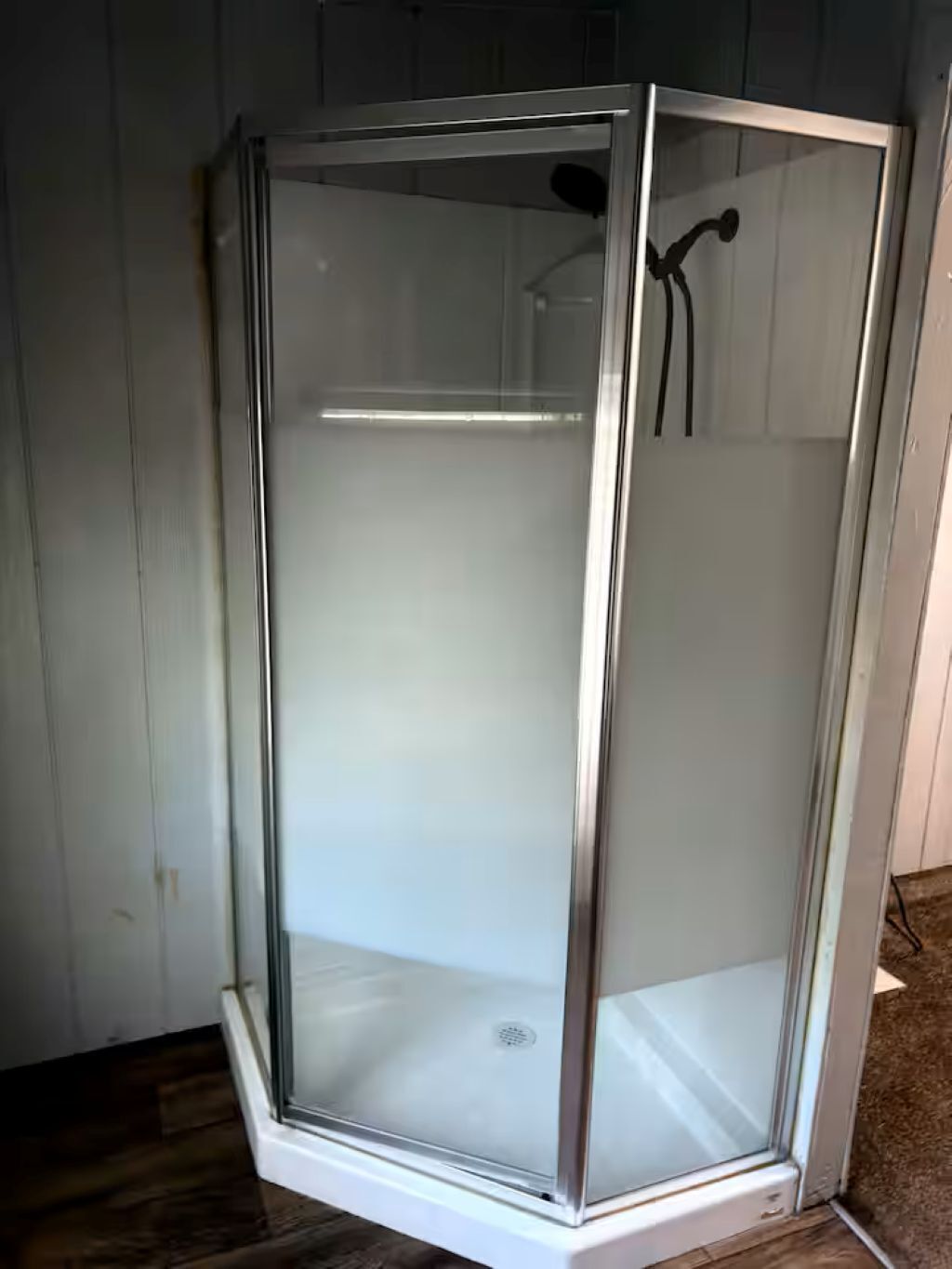 A glass-enclosed shower stall with a white base, a showerhead, and a drain.