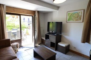 En stue med sofa, sofabord, fjernsyn på et stativ og en skydedør, der fører til et udendørs område med stole.