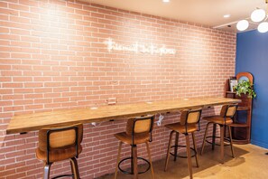 A long wooden table with four chairs, a brick wall, and a neon sign.
