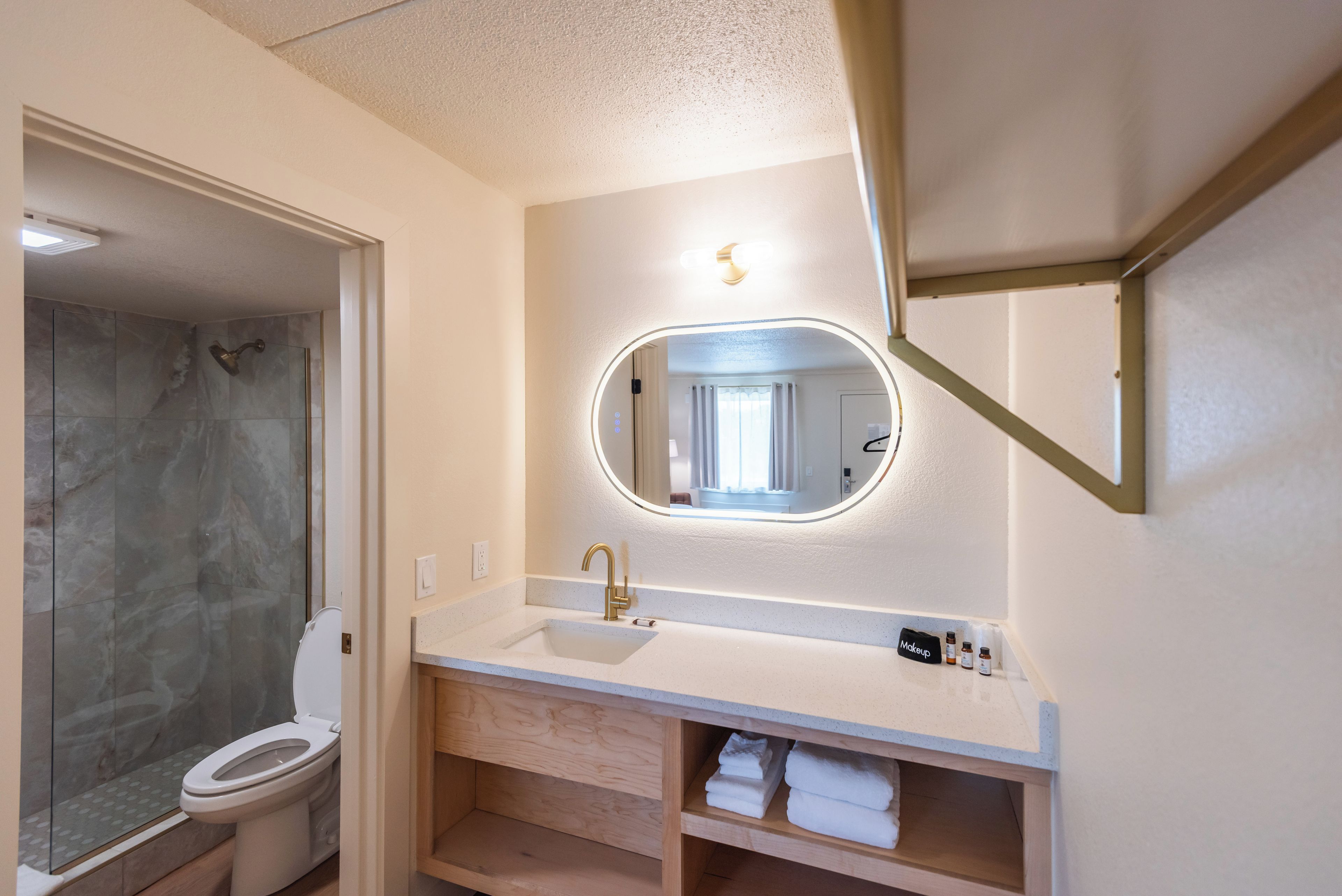 A bathroom with a shower, toilet, vanity with a mirror, and a shelf with towels.