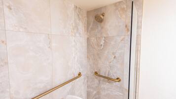 A shower with a handheld showerhead and a glass door.
