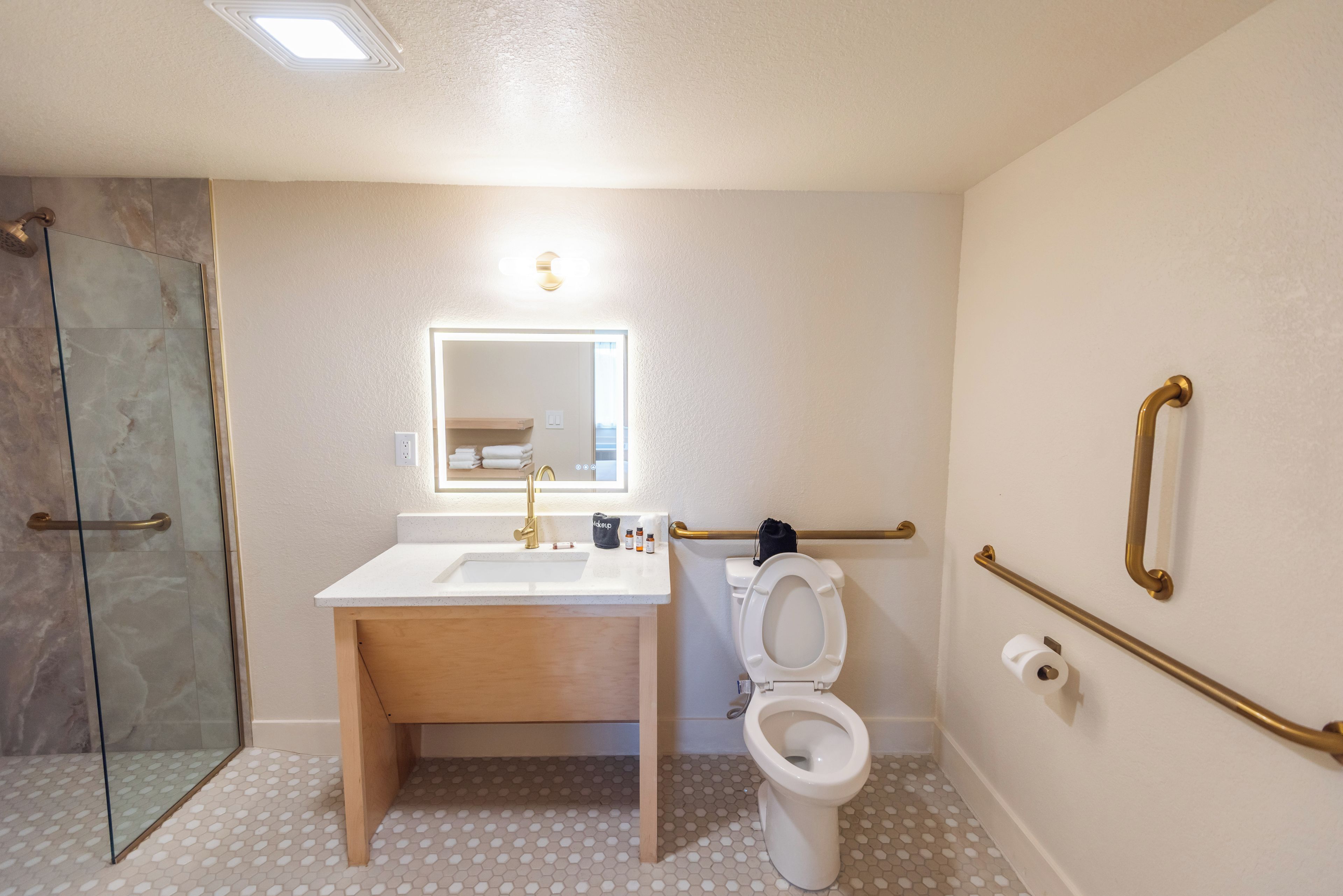 Un baño con cabina de ducha de vidrio, lavamanos con espejo y retrete con barandilla.
