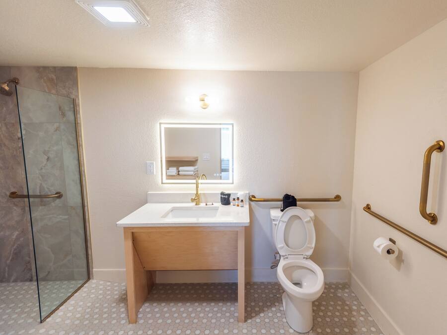 Un baño con cabina de ducha de vidrio, lavamanos con espejo y retrete con barandilla.