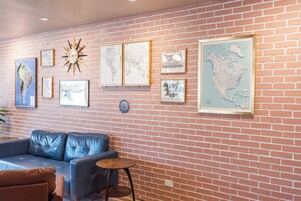 Una habitación con pared de ladrillo, un sofá de cuero azul, una pequeña mesa redonda y varios mapas enmarcados y obras de arte.