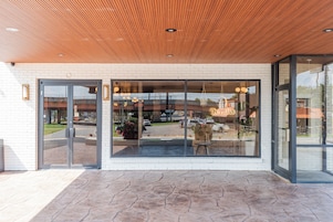 Entrada de un edificio con techo de madera, puertas de cristal y un área pavimentada en el frente.