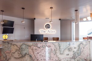 Un mostrador de recepción con un mapa, un cartel que dice 'The Atlas' y un televisor de pantalla plana.