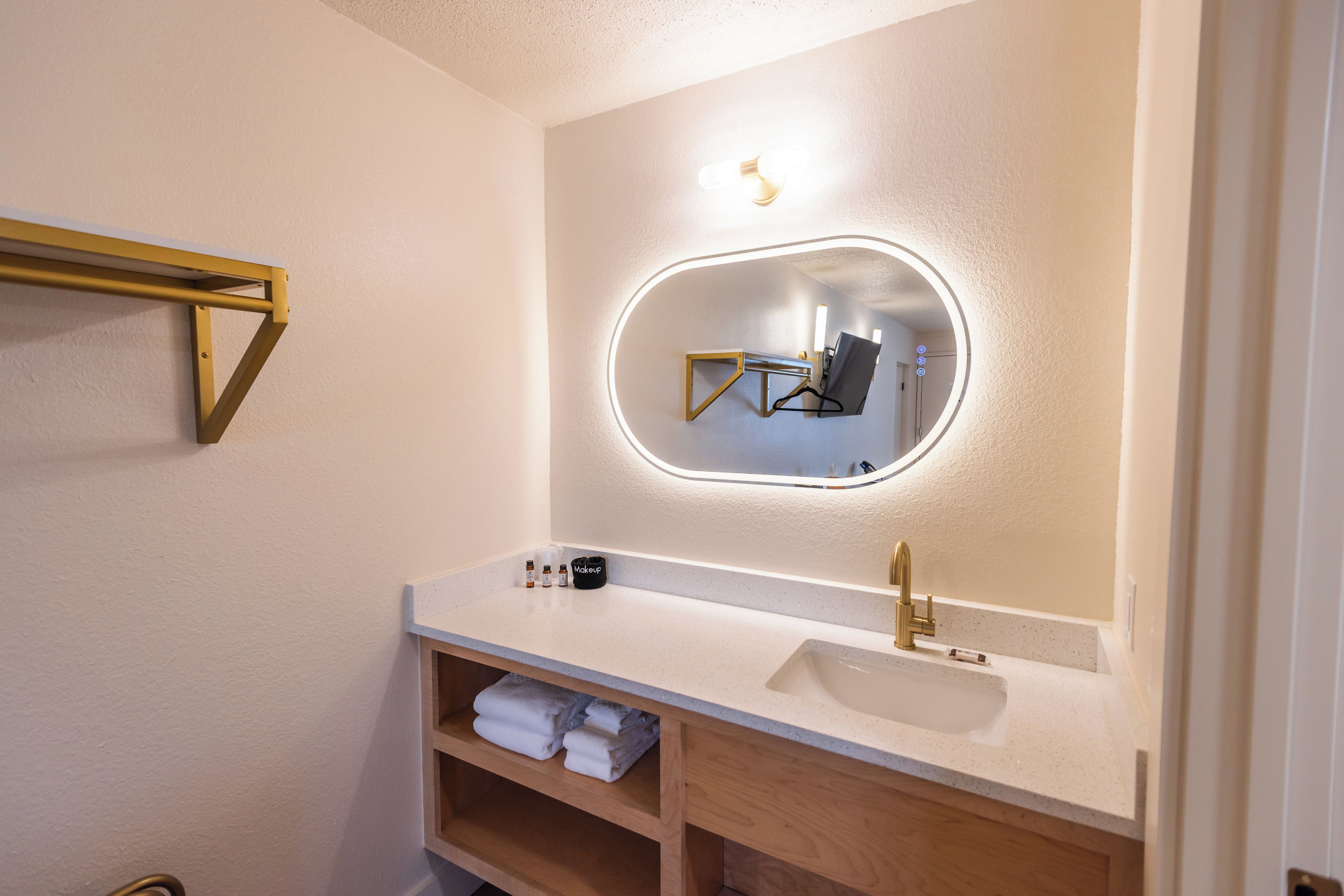 Un baño con un lavabo blanco, un grifo dorado, un espejo con luz y un perchero para toallas.