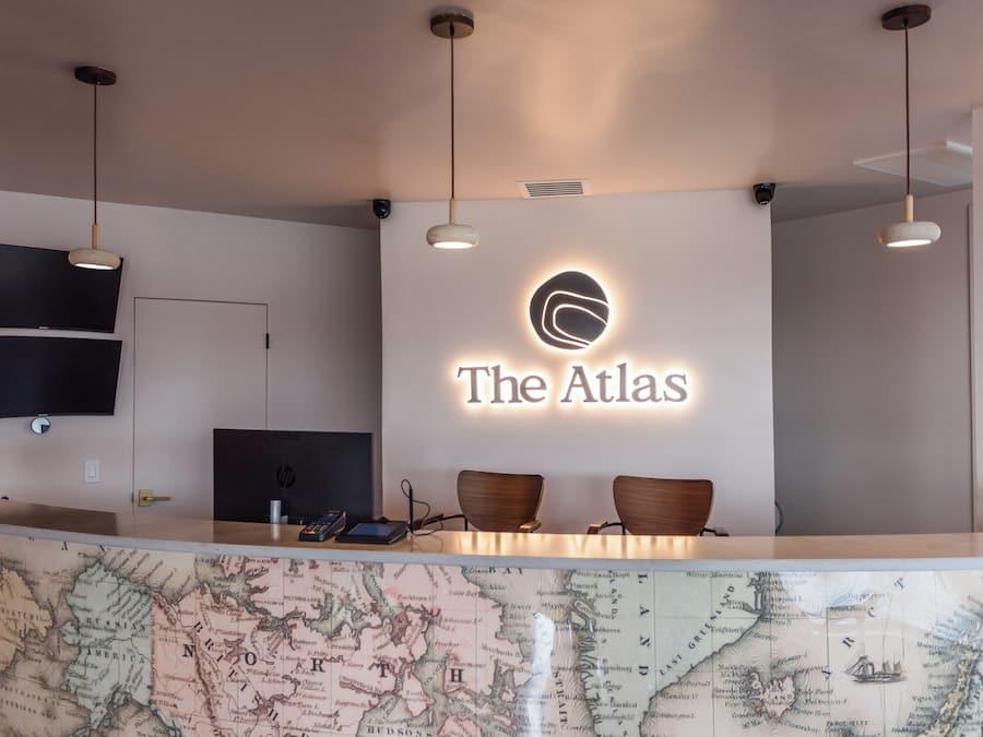 A reception desk with a map, a sign reading 'The Atlas,' and two wooden chairs.