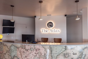 Un mostrador de recepción con un mapa, un cartel que dice 'The Atlas' y dos sillas de madera.